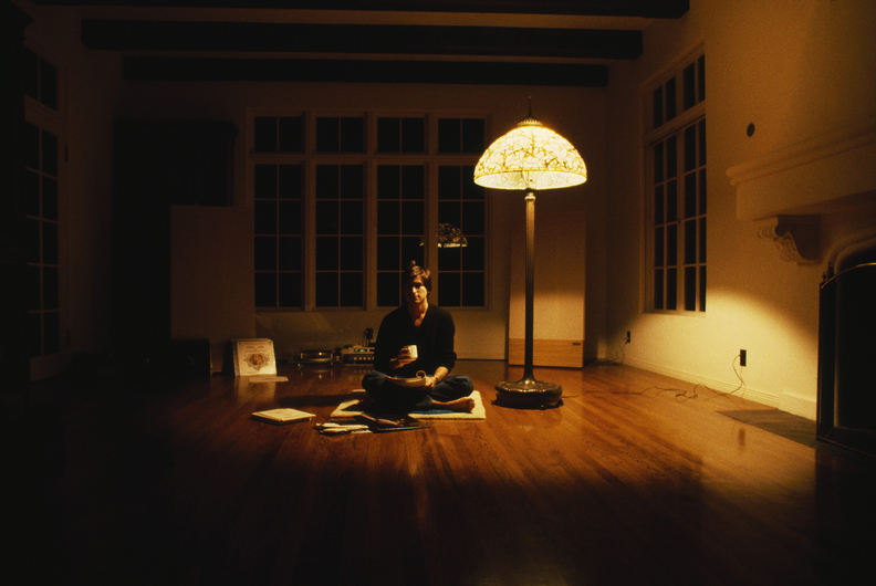 The meme depicts a person sitting on the floor with their legs crossed, surrounded by various electronics and snacks. The image is captioned "I'm not lazy, I'm just on energy-saving mode".